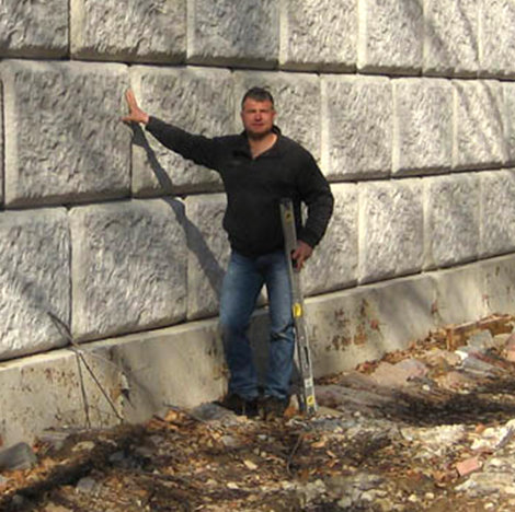 Man holding a level, leaning on a stone wall
